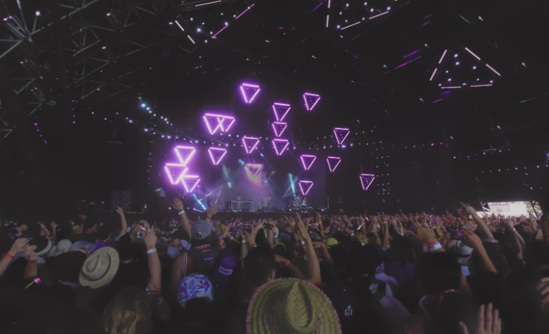 Vibrant crowd at Coachella music festival enjoying a performance under a canopy of neon-lit geometric shapes, showcasing this world-famous festival's cutting-edge artistry and exclusivity.