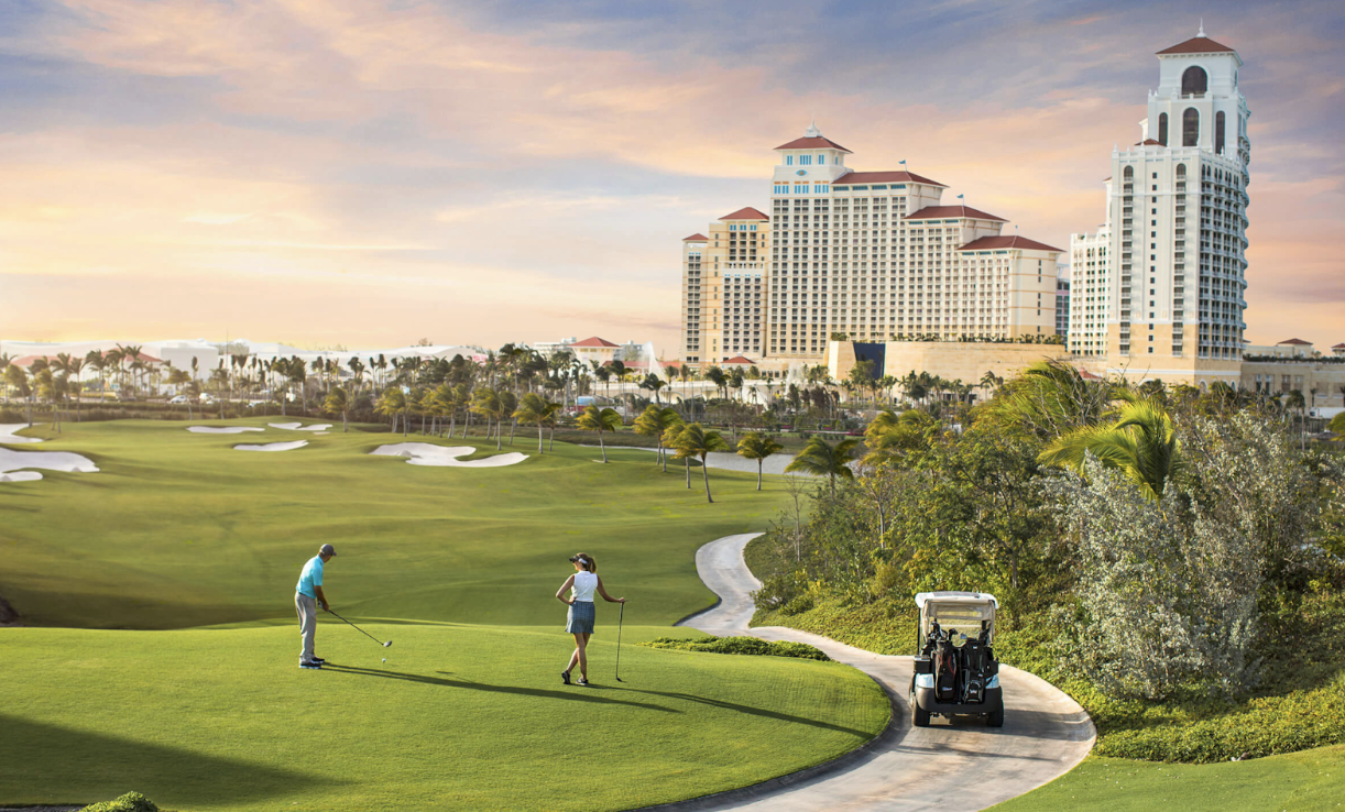 A mesmerizing setting of the Royal Blue Course Alt text: A scenic golf course bathed in golden sunlight featuring lush fairways, palm trees, and a luxurious resort in the background. While an elegant couple enjoys a round of golf, a sleek golf cart awaits in the setting of exclusivity and sophistication.