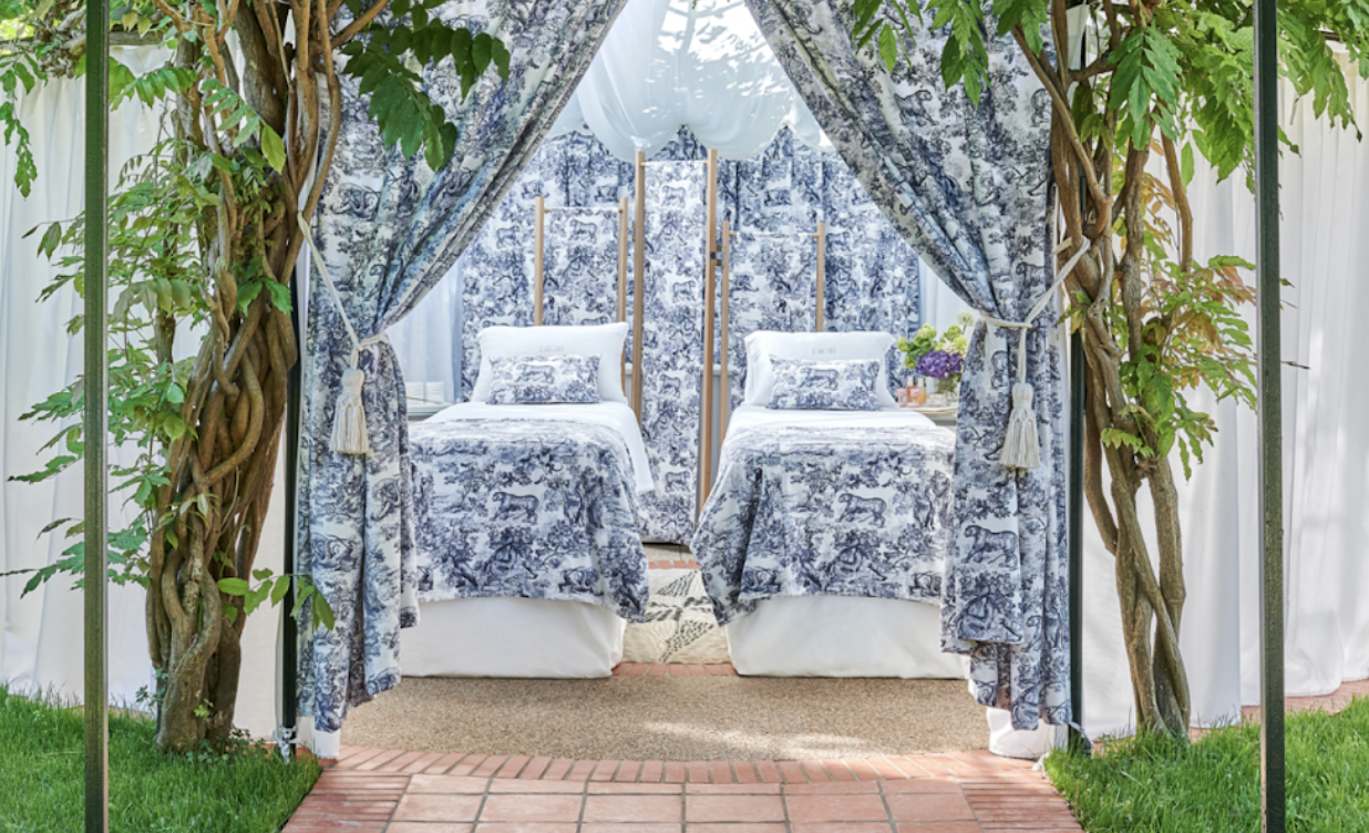 A treatment room at the Spa, a gazebo in the garden    Alt Text: Framed by lush greenery and entwined vines, this serene outdoor treatment room is draped in blue-and-white toile fabric featuring two spa tables with matching linens.