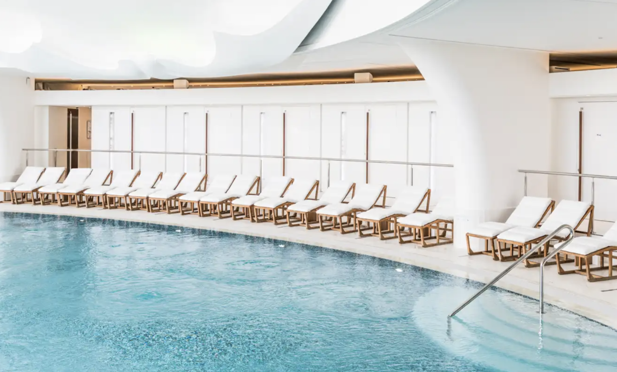 A serene pool at Thermes Marins Monte-Carlo, surrounded by elegant white chairs, creates a tranquil atmosphere for guests to unwind.