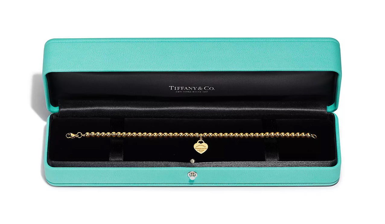 A mesmerizing signature Tiffany blue box shows a pristine gold bead bracelet with an engraved heart pendant.