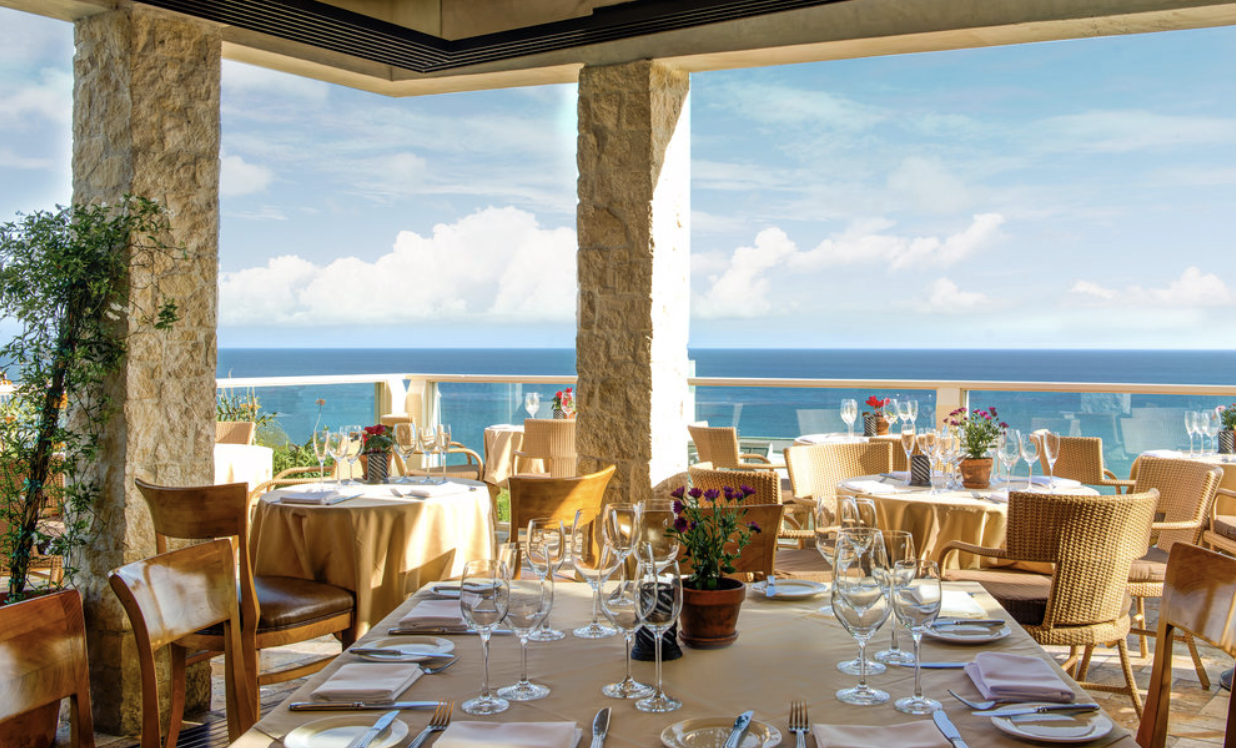 Sunlit balcony dining area overlooking the azure water of the Pacific coastline.