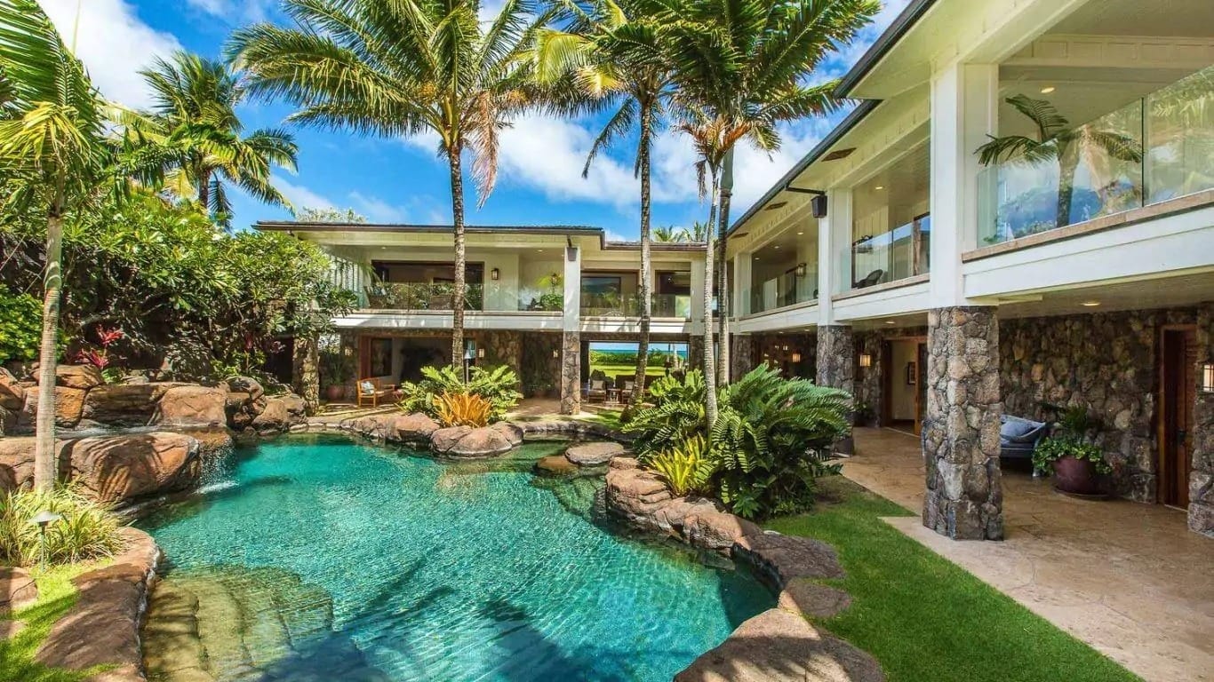 Royal Kailua Estate in Hawaii features a lagoon-style pool, lush tropical landscaping, and elegant stone architecture. A luxury vacation rental near top golf courses in Oahu.